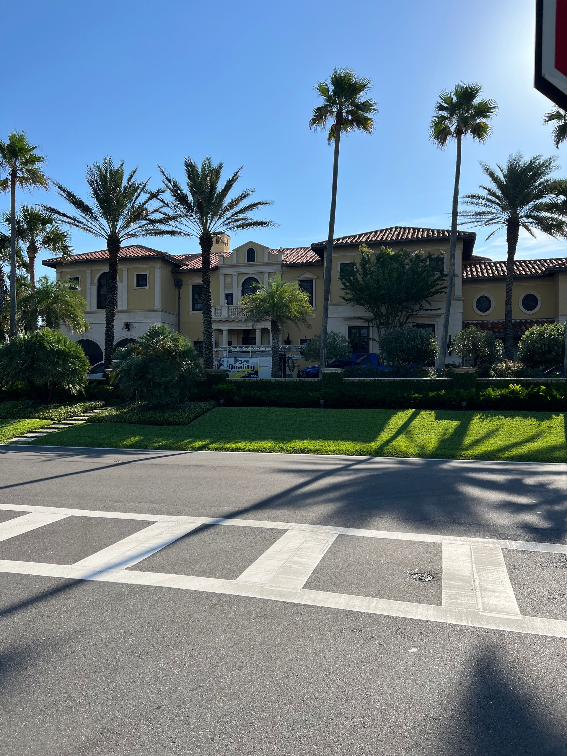 Large yellow building with red-tile roof, palm trees, and crosswalk in front.
