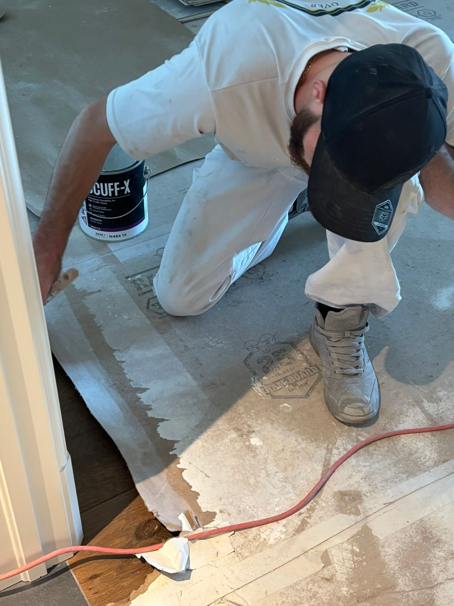 Worker kneeling on a floor, smoothing wet concrete beside a cord and an outlet.