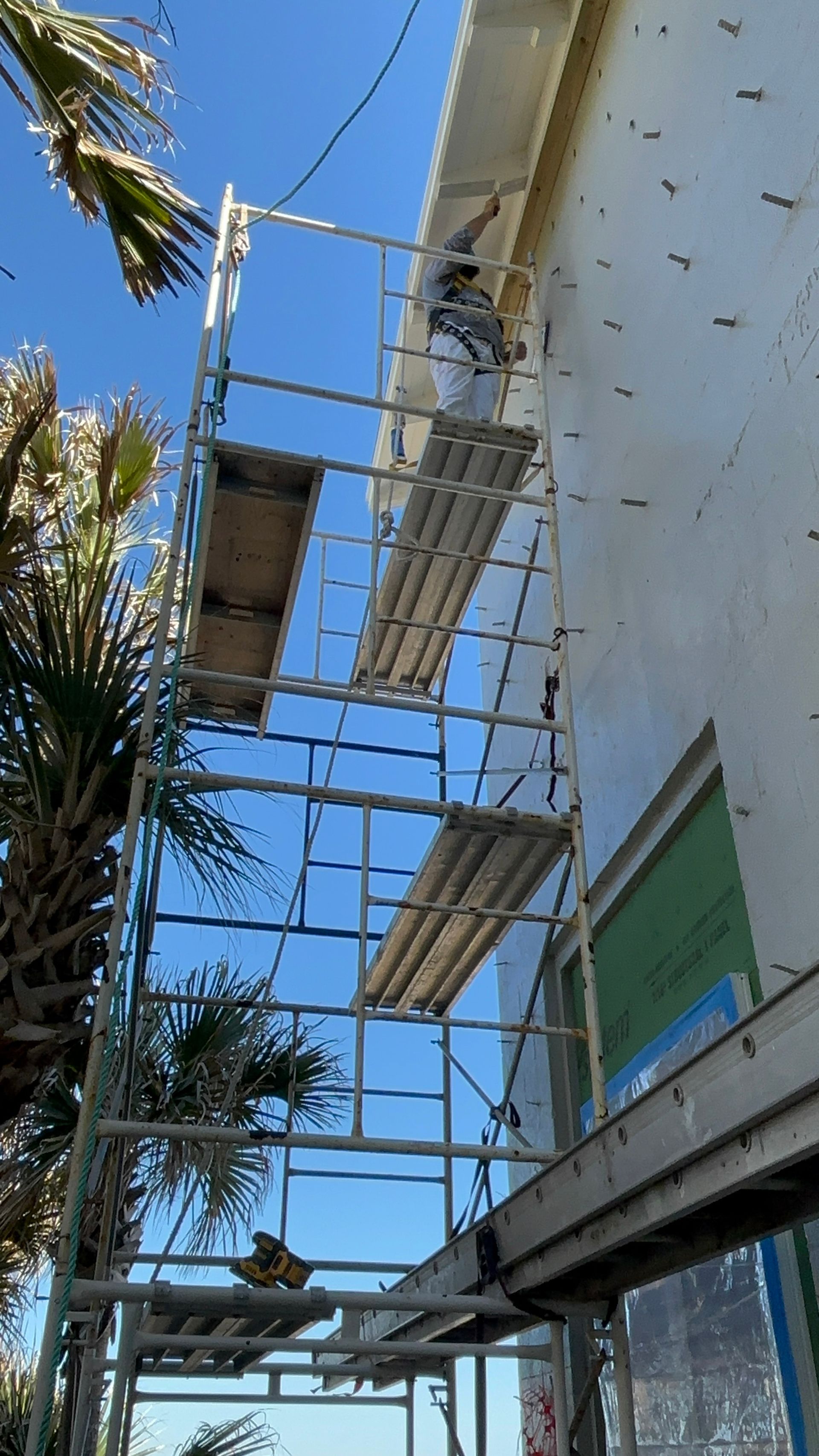 Person on scaffolding painting exterior of a building, blue sky backdrop.
