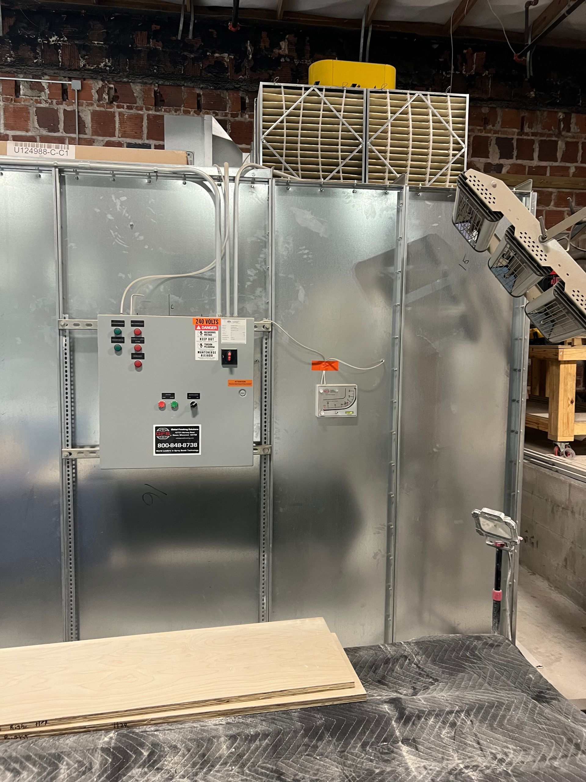 Metal HVAC unit with control panel, pipes, and fan against a brick wall.