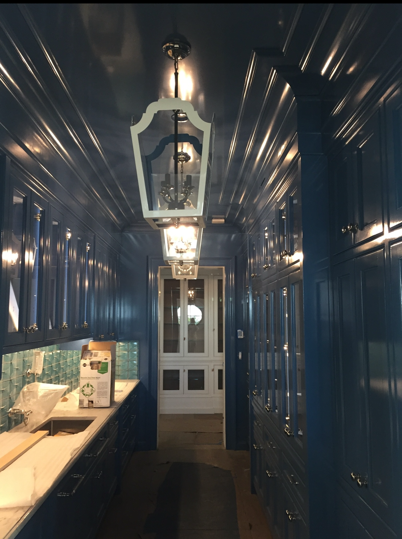 Navy blue, glossy hallway with hanging lanterns, cabinets, a sink, and a door at the end.