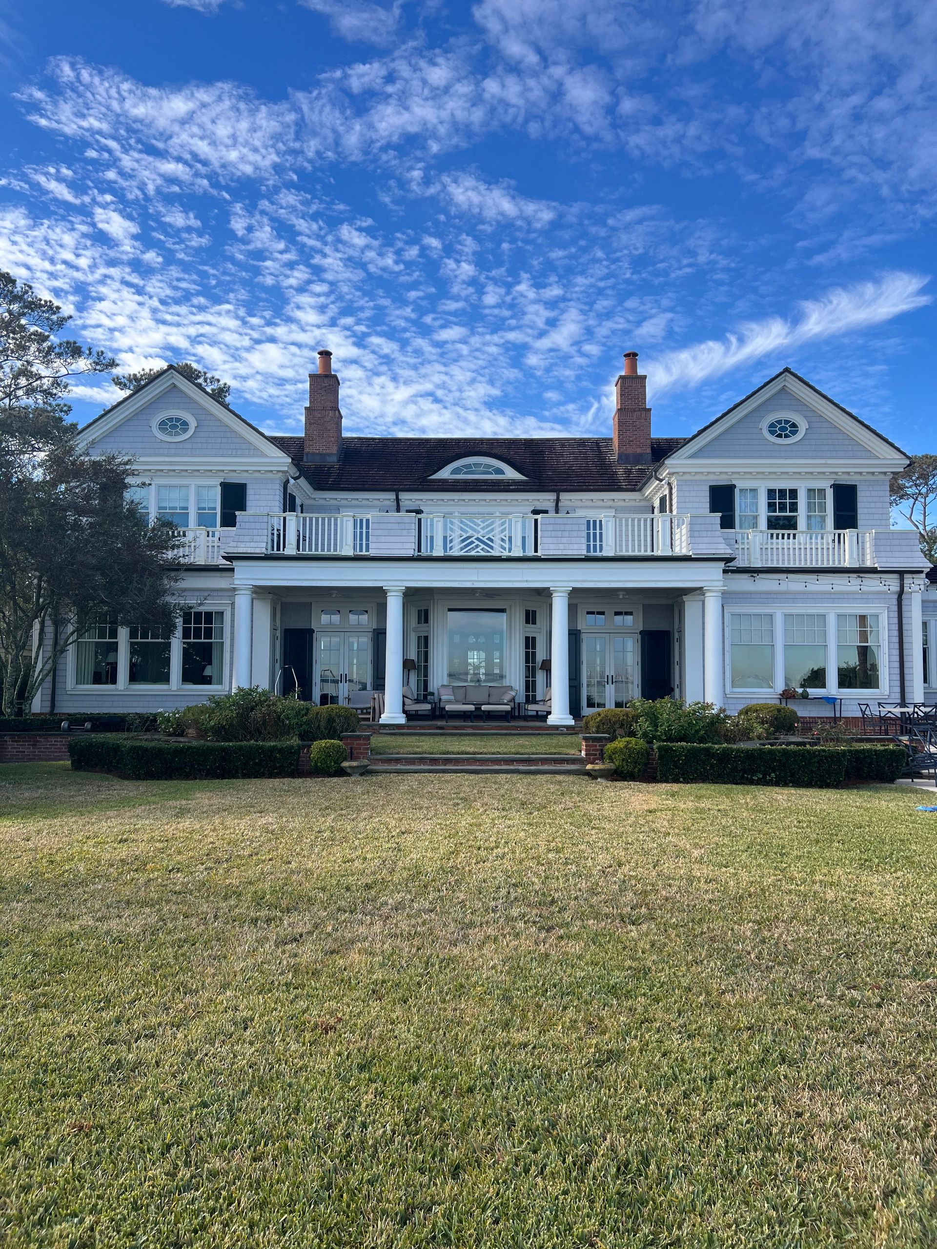 Large gray house with white columns, on a grassy lawn under a blue sky.