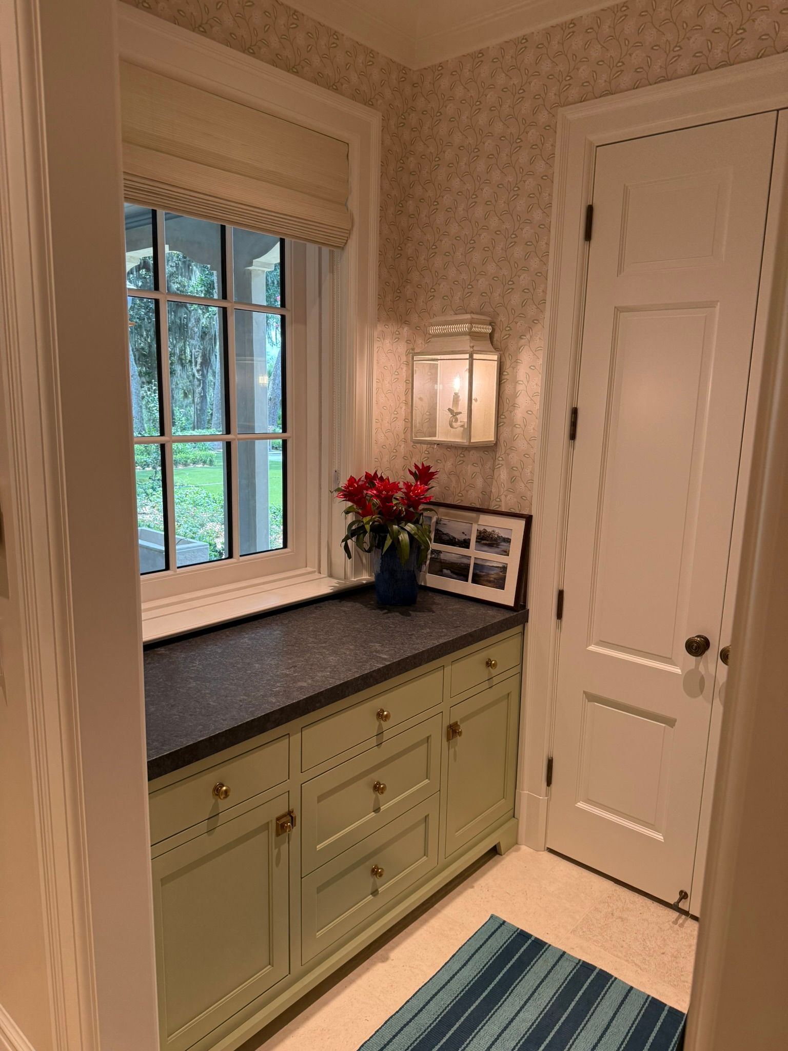 Small hallway with green cabinet, granite counter, window, floral wallpaper, and white door.