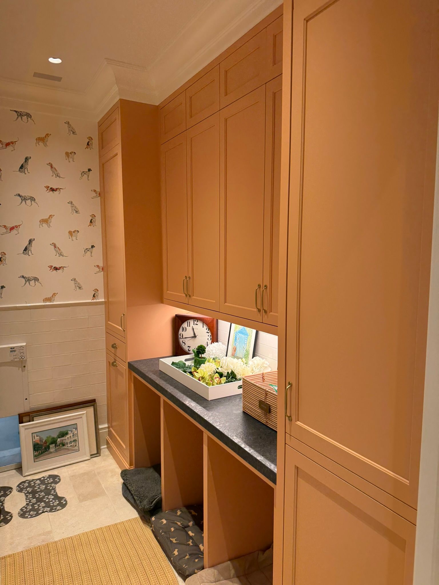 Orange built-in cabinets and a small counter in a tiled room with patterned wallpaper and a plush toy.