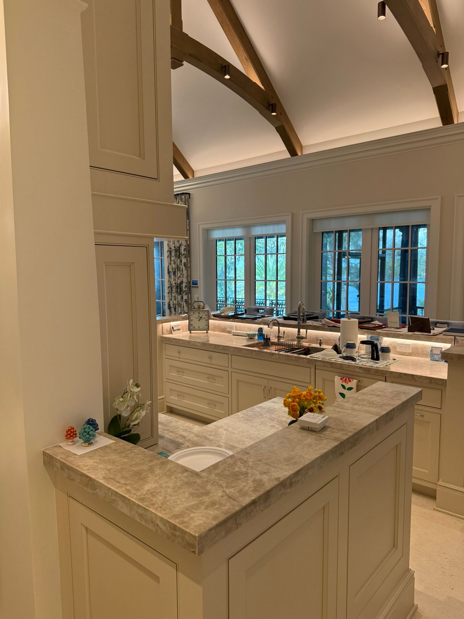 Bright kitchen island with marble countertops, white cabinetry, and tall windows in a vaulted room