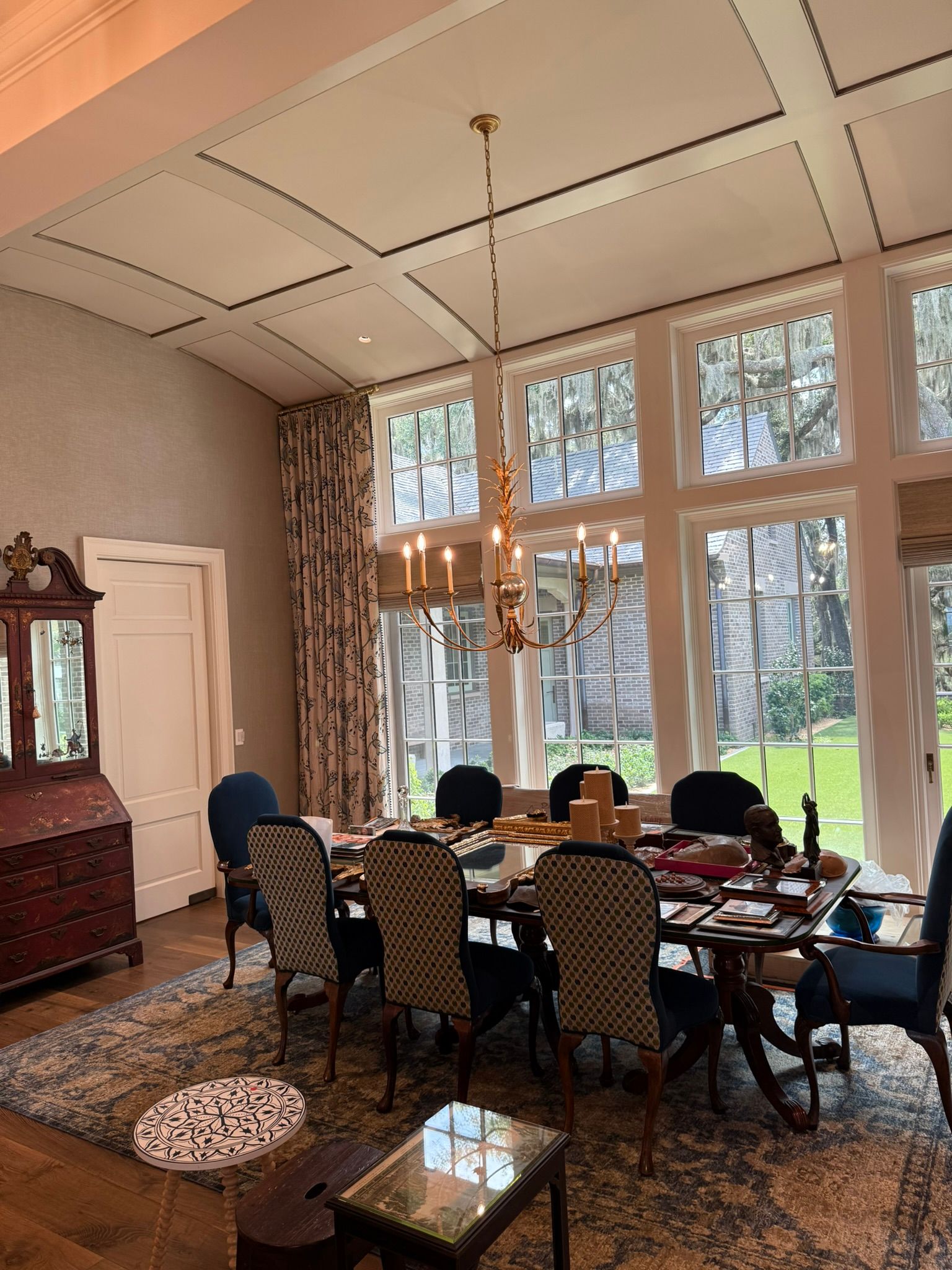 Dining room with a long table, patterned chairs, and large windows overlooking a green yard.