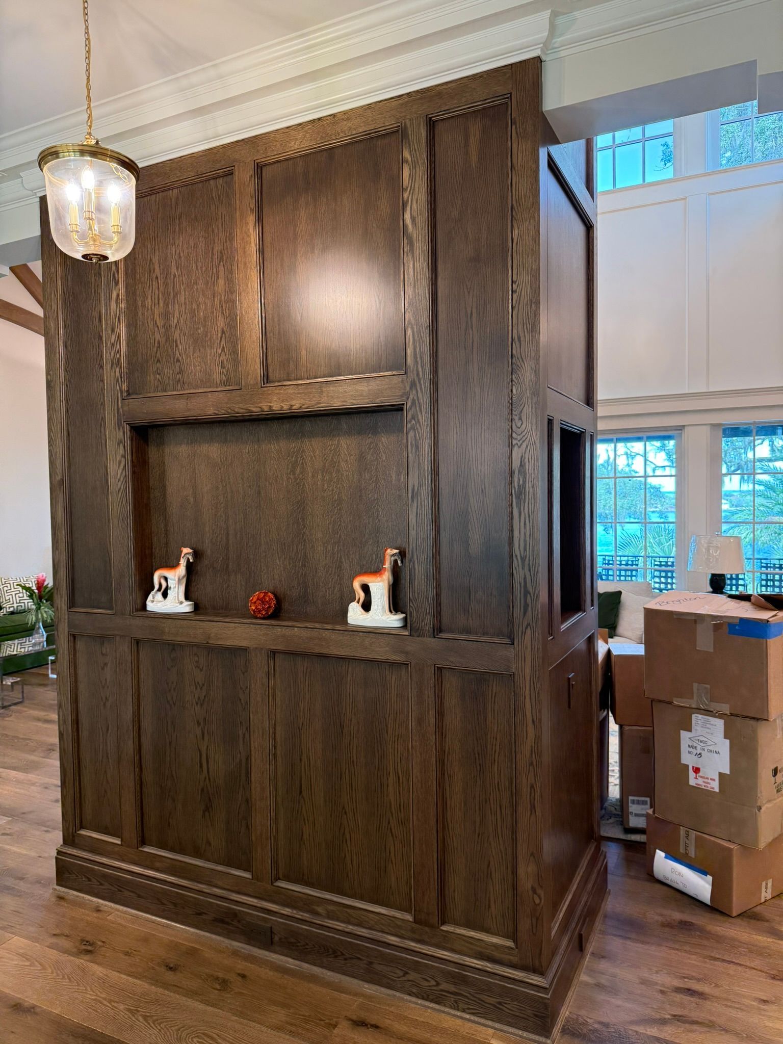 Dark wood built-in shelving and cabinet in a bright room, with boxes stacked by the window.