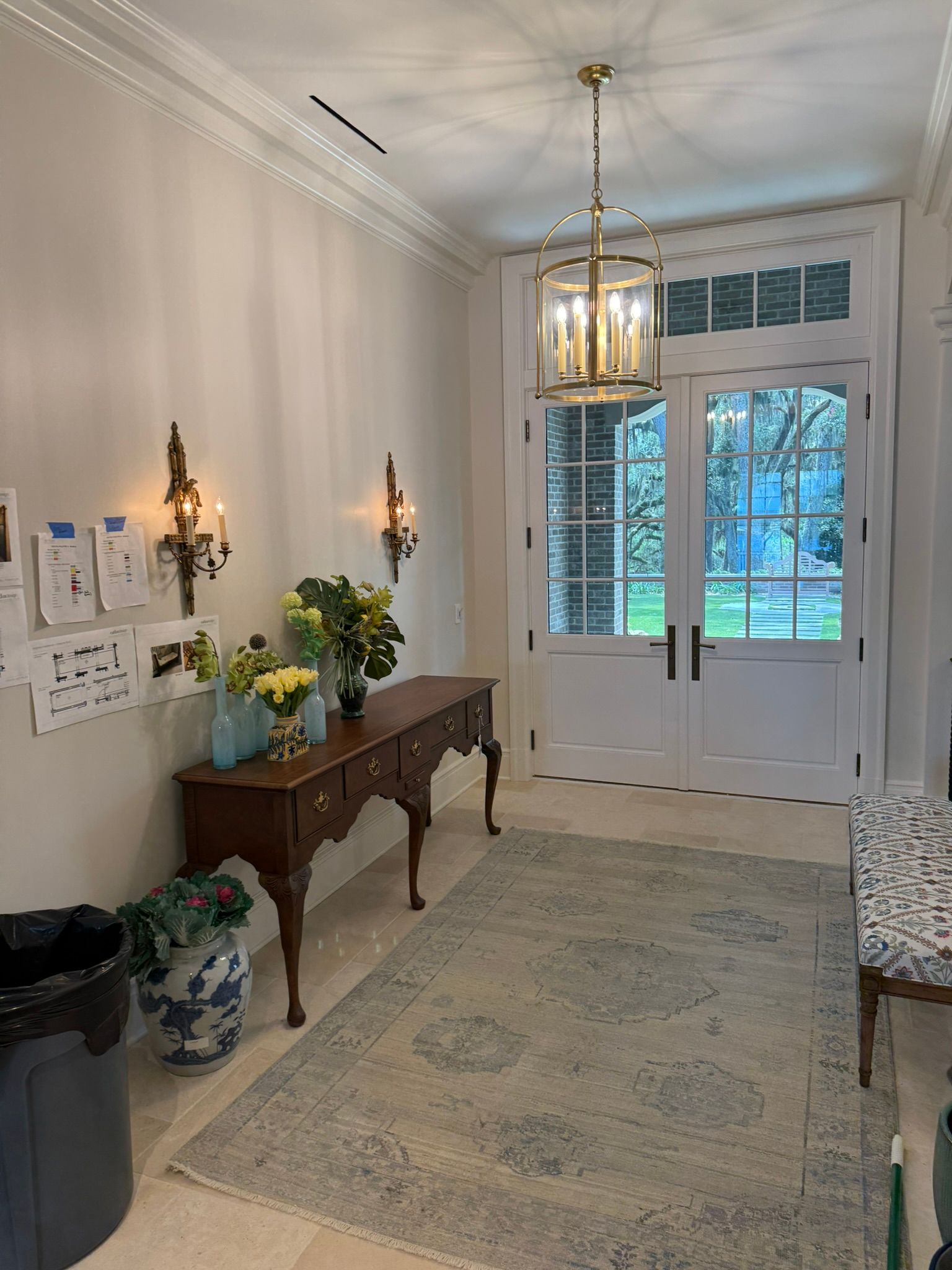 Bright hallway with console table, flowers, wall sconces, rug, and white double doors opening outside