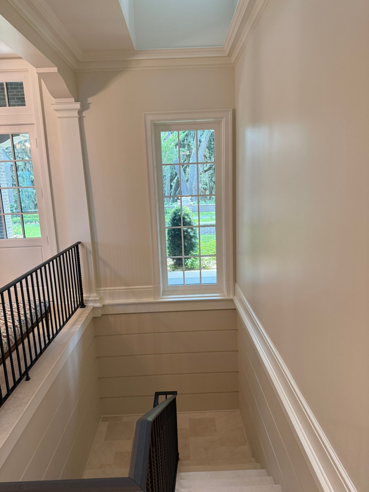 Elegant staircase landing with cream walls, black railing, and a window overlooking greenery