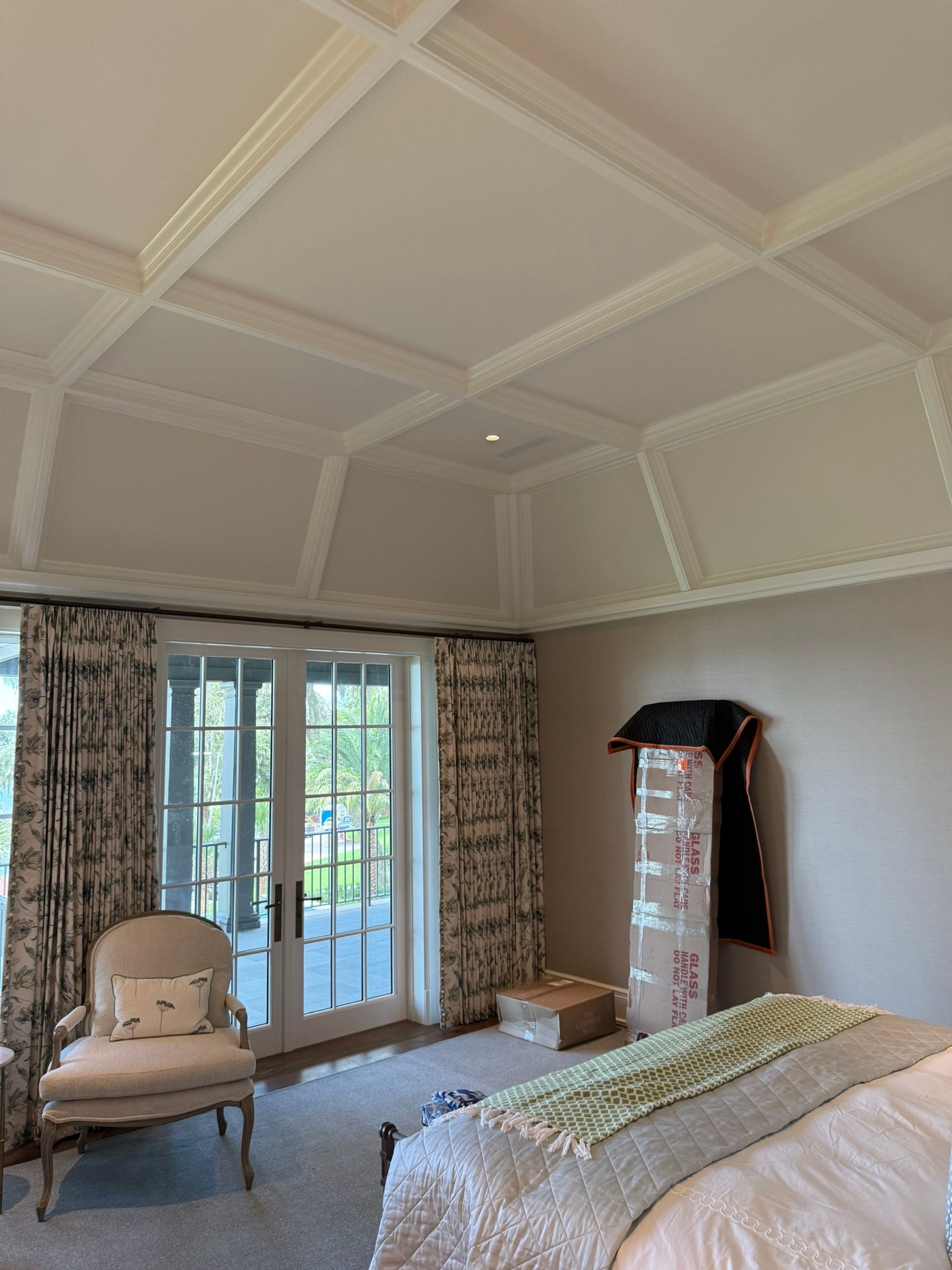 Bedroom interior with coffered ceiling, French doors, patterned curtains, and a bed.