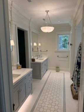 Bright white bathroom with double vanity, long patterned runner, and small window at the far end.