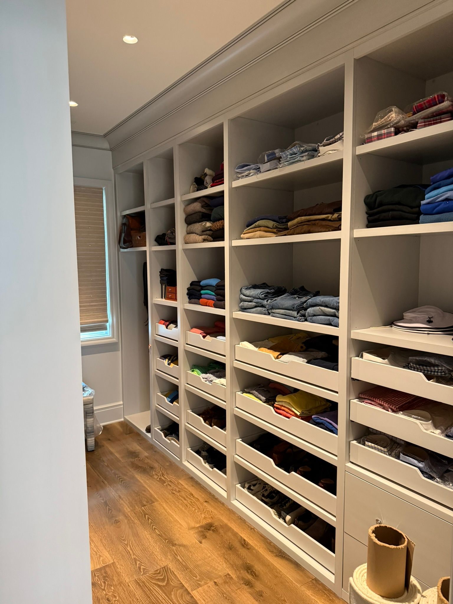 Walk-in closet with open shelving, folded clothes, and a wooden floor along a narrow hallway.