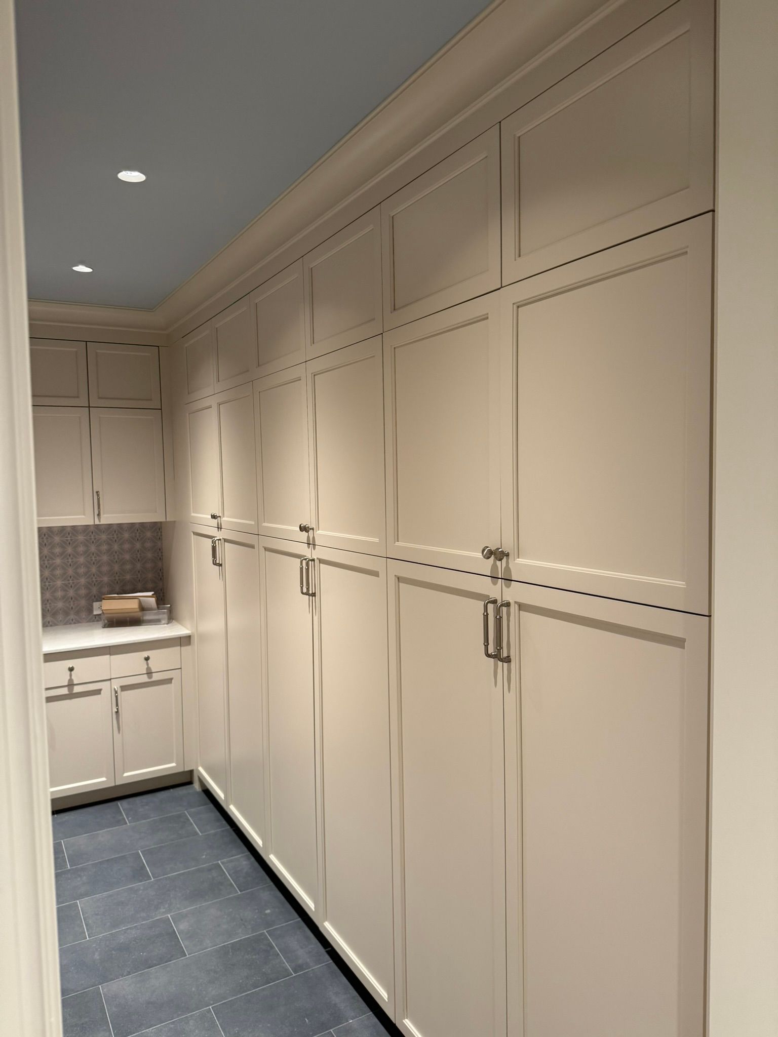 Narrow hallway with beige built-in cabinets, brass pulls, and dark blue floor covering.