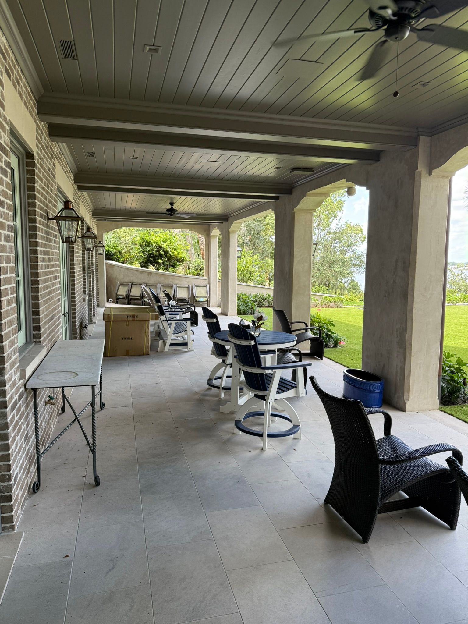 Covered patio with stone columns, outdoor furniture, and ceiling fans overlooking a yard.