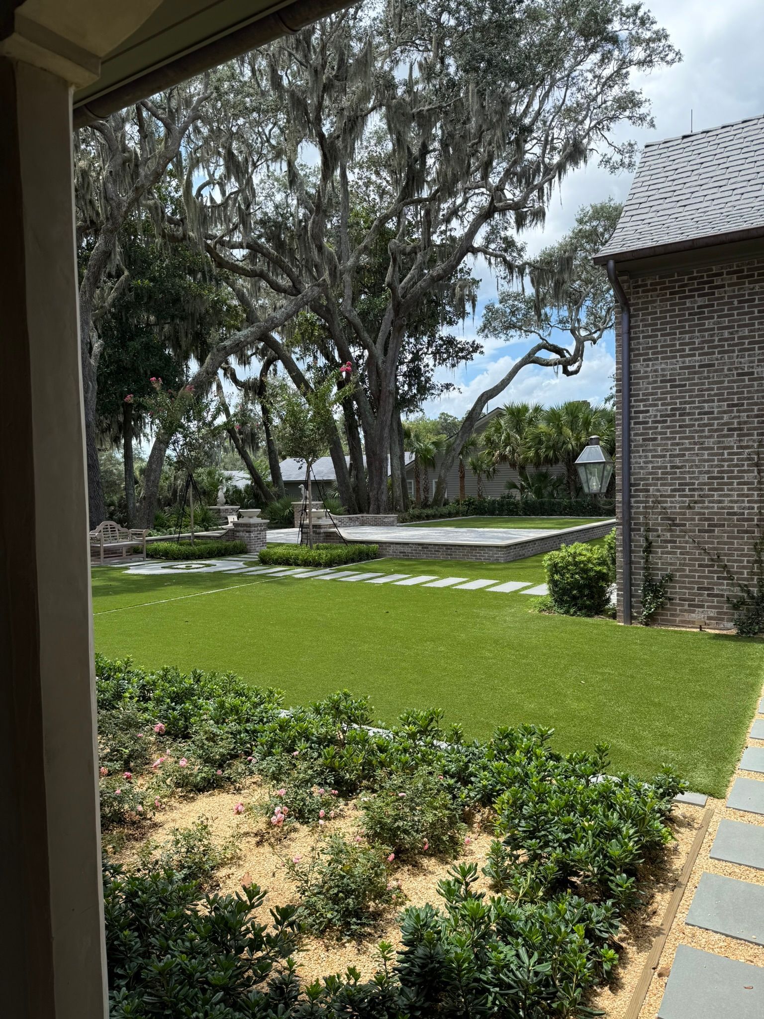 Green lawn and landscaped trees beside a paved walkway under a bright sky