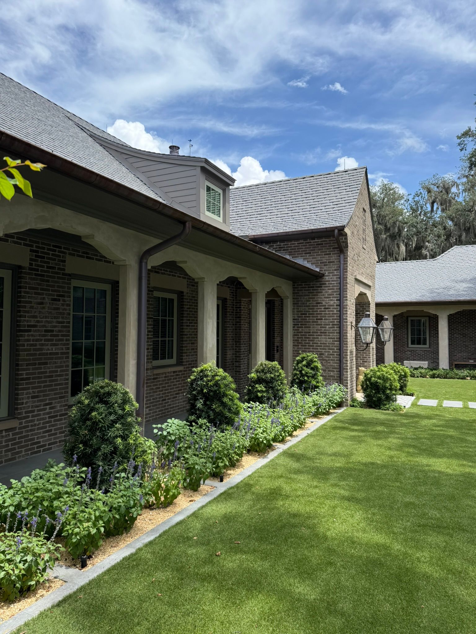 Stone house with striped roof overhang, arched windows, and a neatly landscaped green lawn under a blue sky