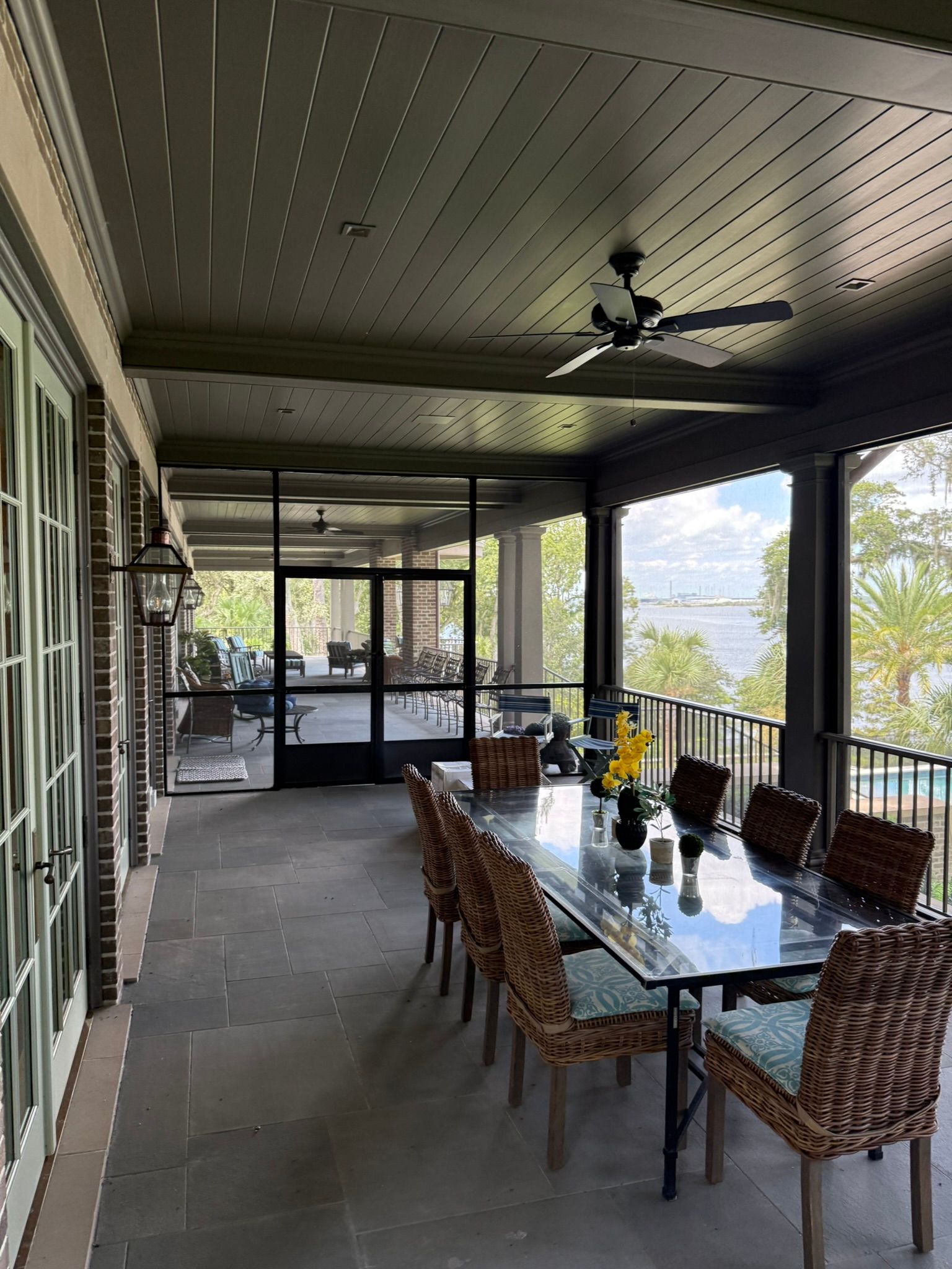 Covered patio with a glass dining table, wicker chairs, and a ceiling fan overlooking trees and mountains.