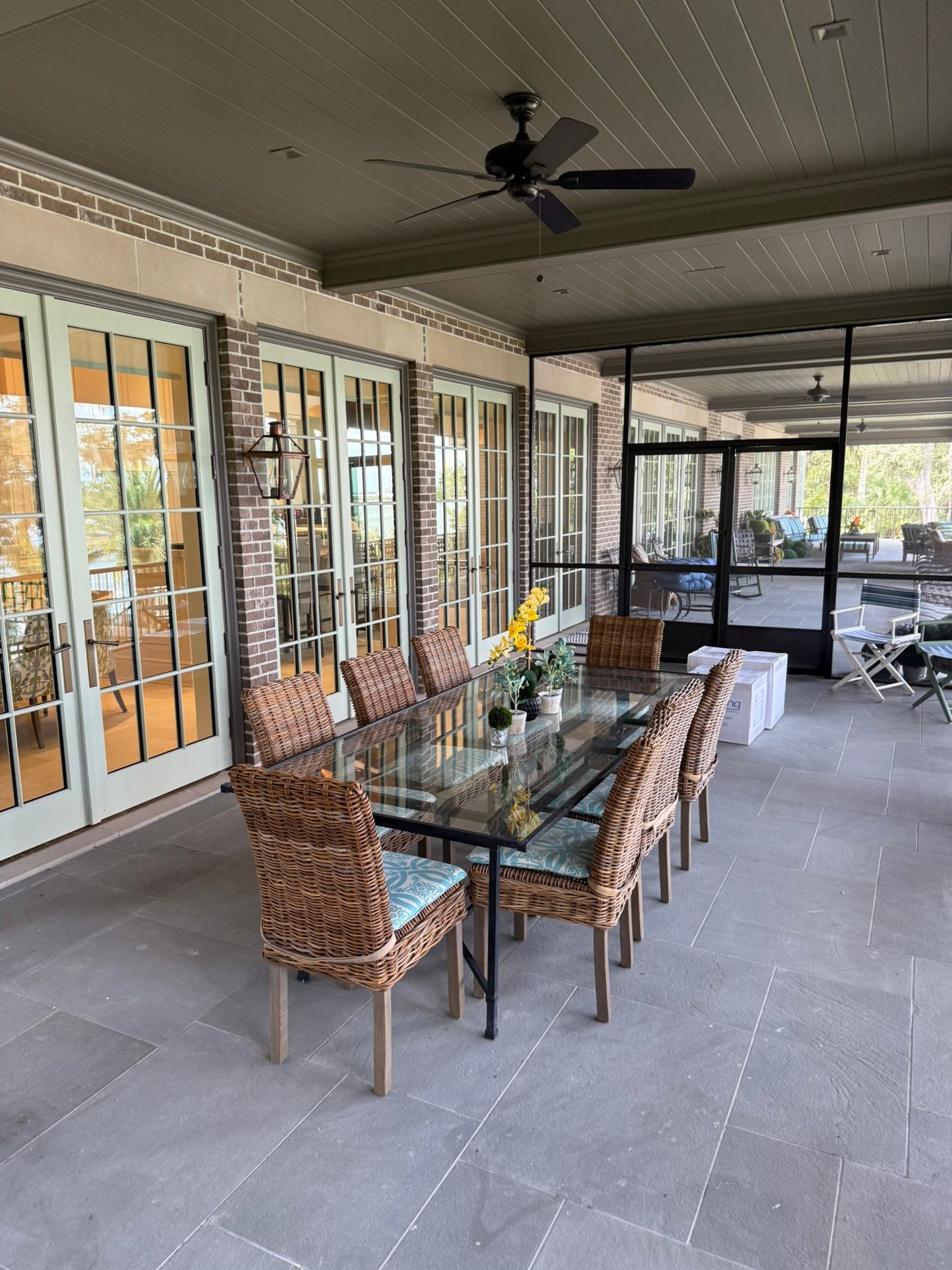 Outdoor dining area with a glass-top table, wicker chairs, and open glass doors.