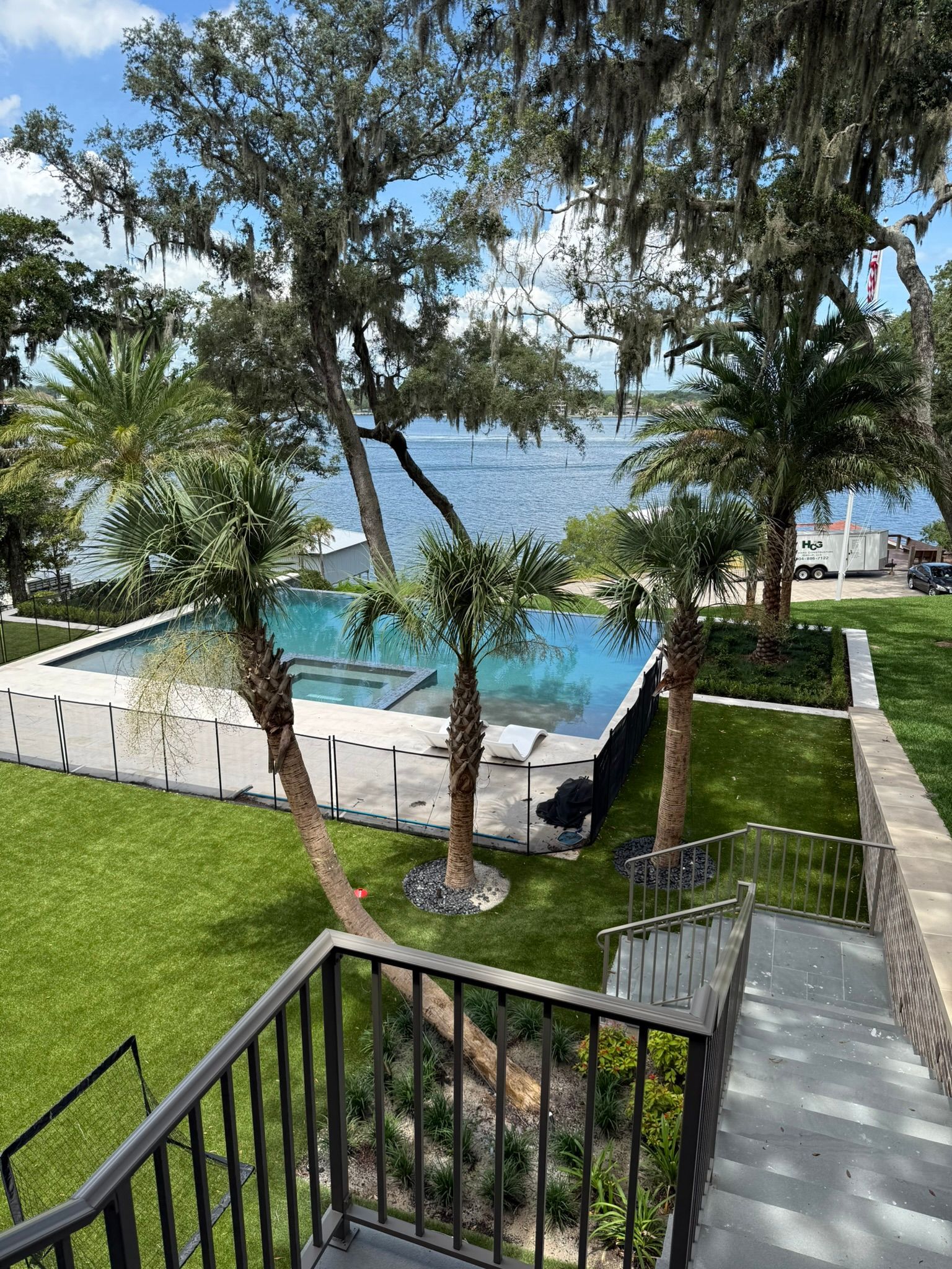 Tropical resort pool with palm trees, ocean view, and a paved walkway overlooking green lawn