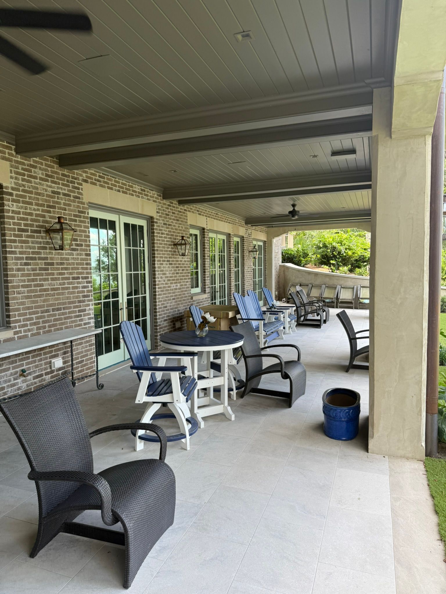 Covered patio with wicker chairs, table, and grill beside a brick house