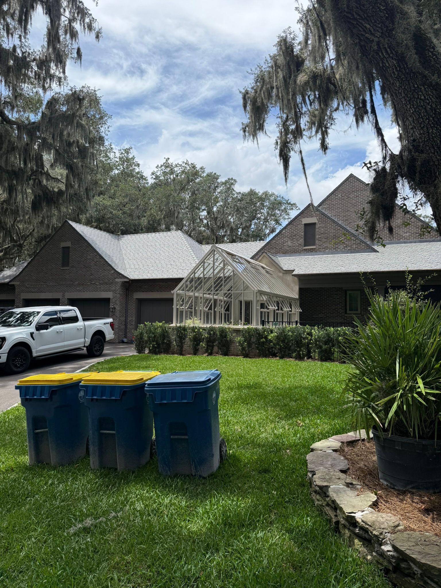 Blue trash bins on a grassy lawn in front of houses, with a white truck and trees in the background.