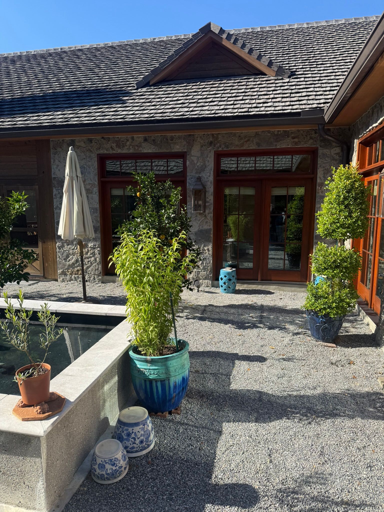 Stone-walled building with wooden doors, a gravel patio, and potted green plants in front.