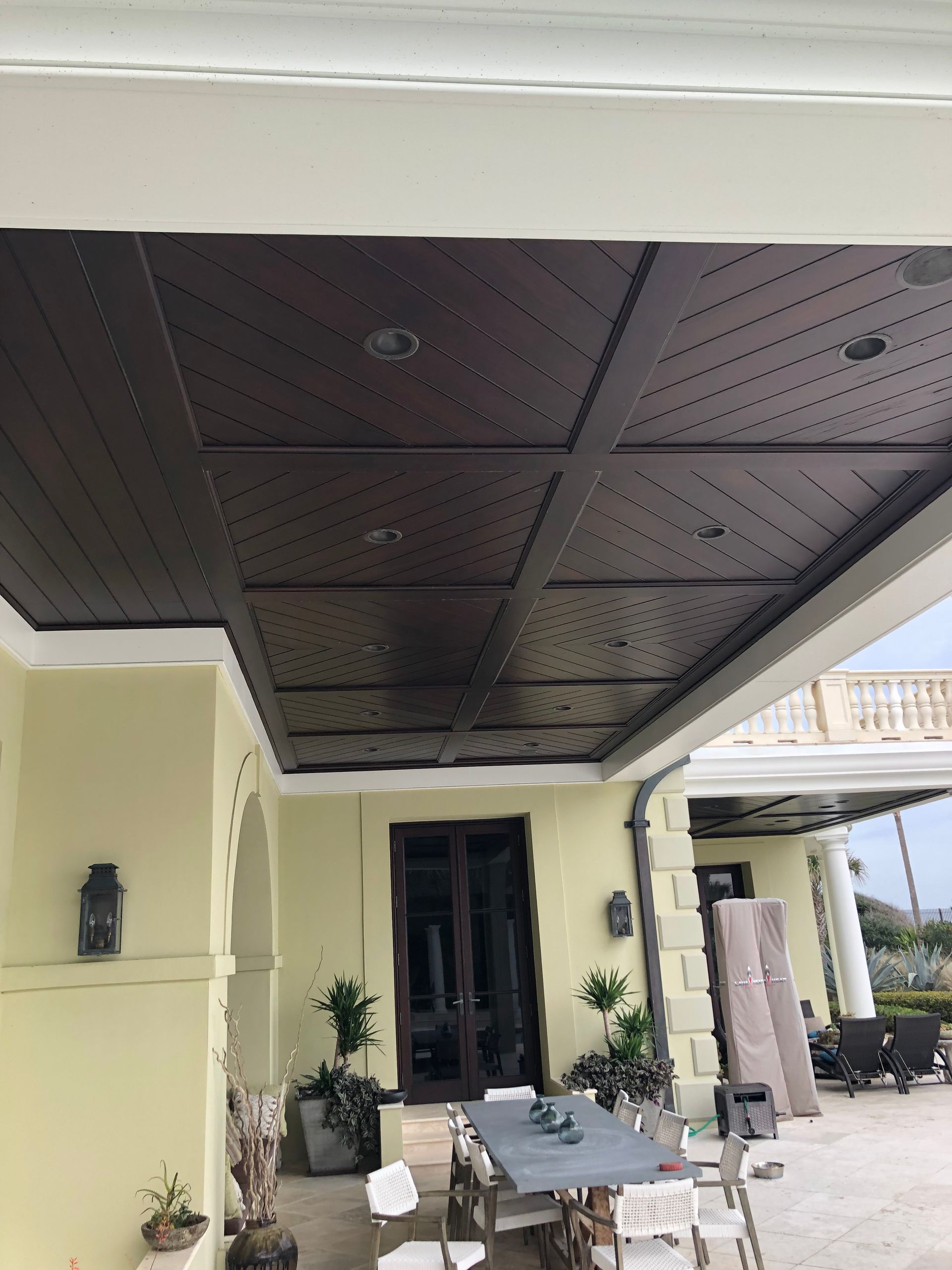 Outdoor patio ceiling with dark wood panels and recessed lighting, tan walls.