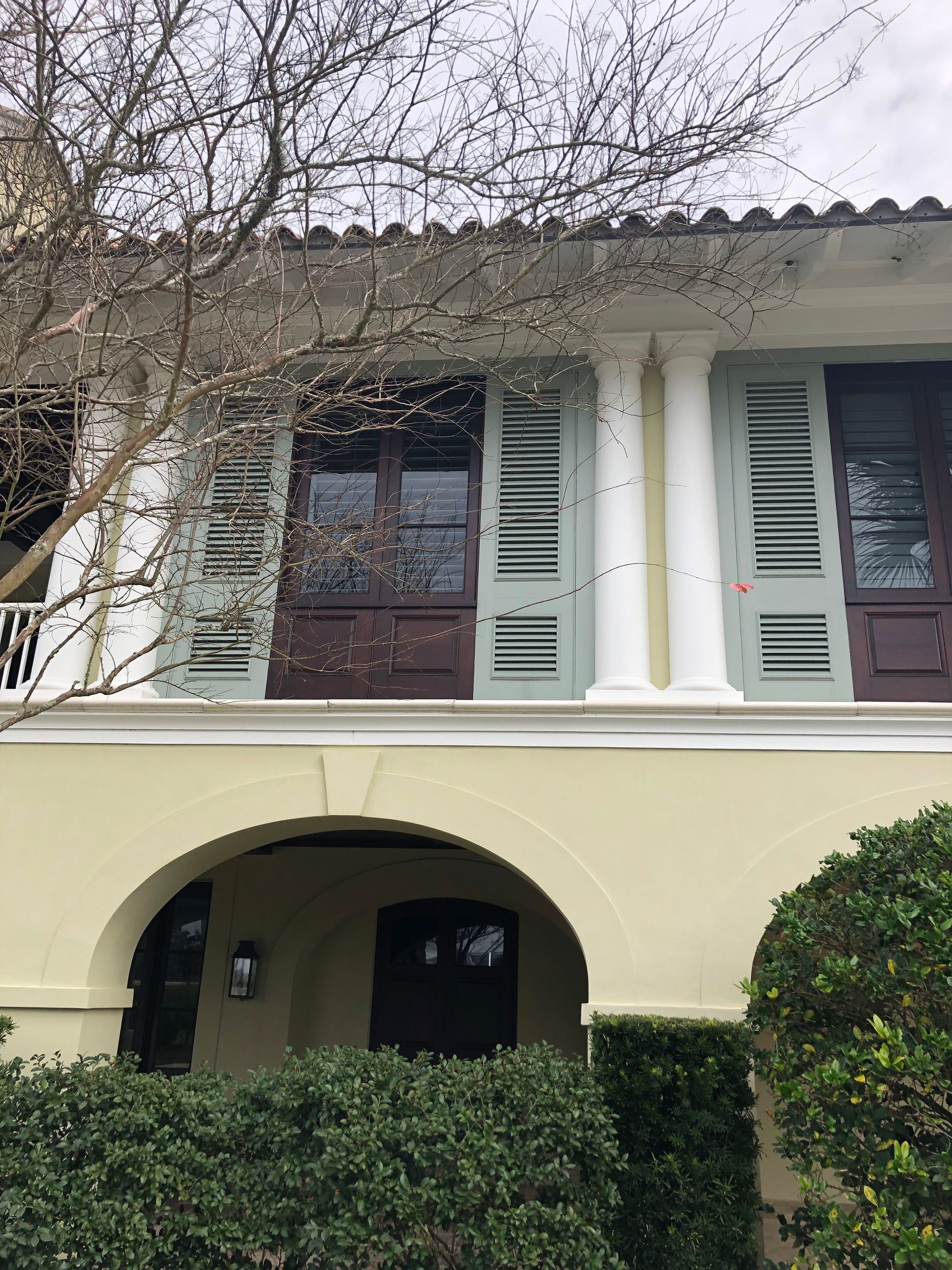 Two-story building with arched entrance and shutters.  Pale yellow exterior, dark brown doors, pale green shutters.