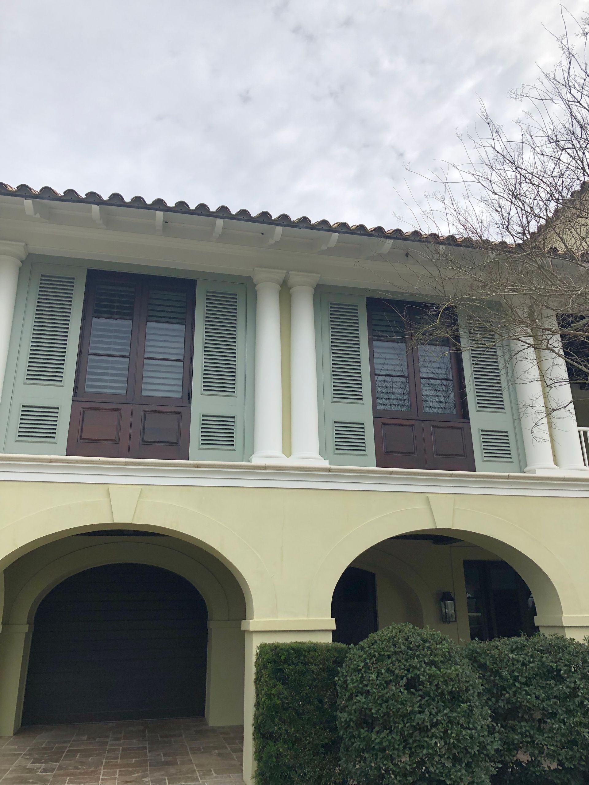 Yellow building with arched entryways, brown doors, blue-green shutters, and white columns.