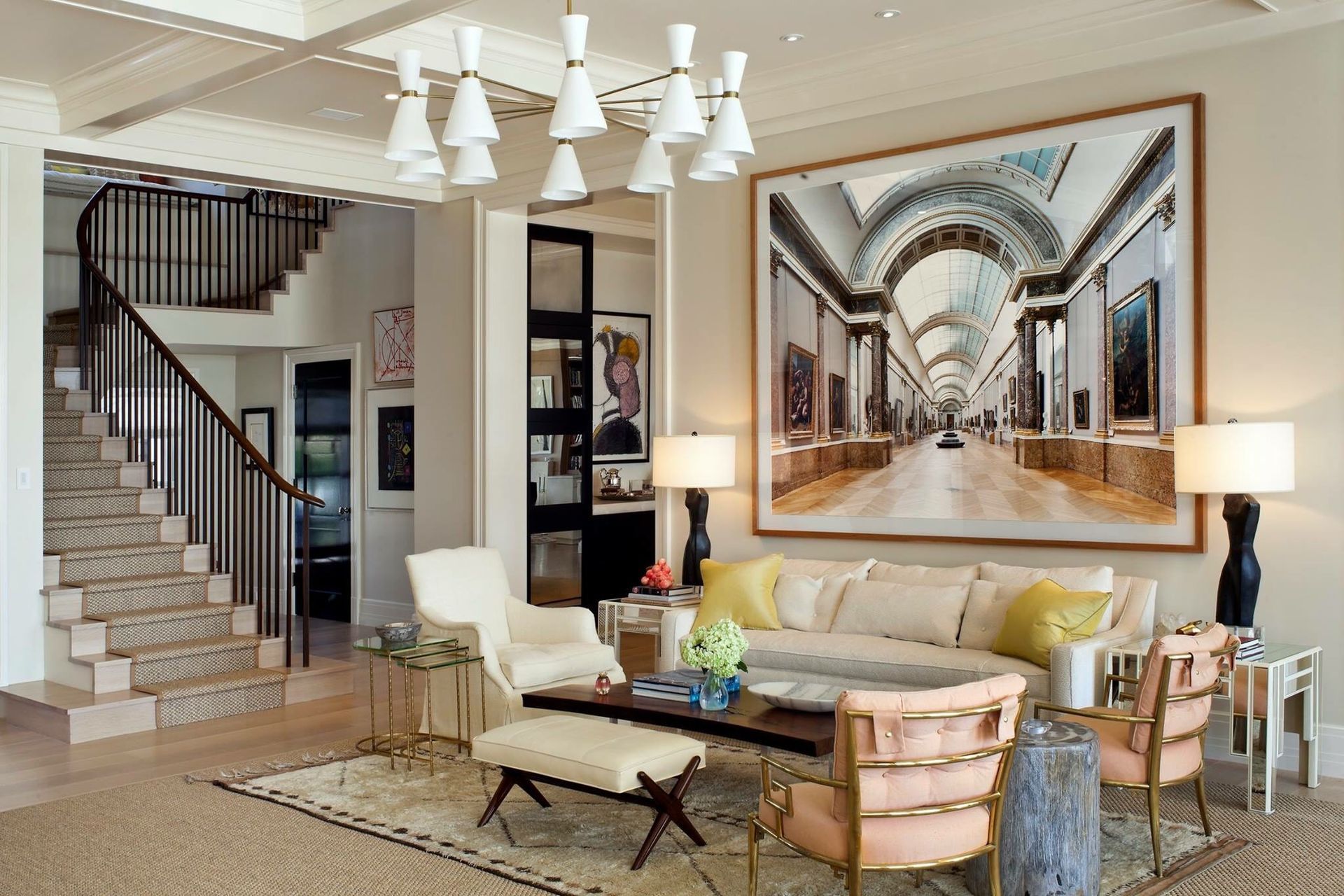 Elegant living room with staircase, large artwork, cream and gold color palette.
