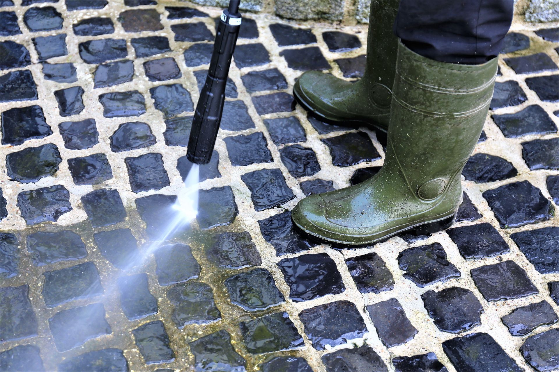 Person in green boots using a cane on a cobblestone street with sunlight glare