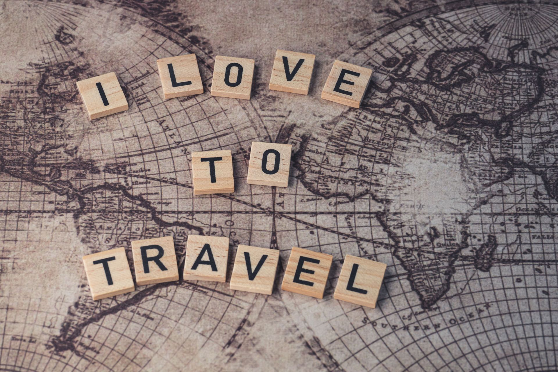 Wooden letter tiles spelling “I love to travel” on a vintage world map background