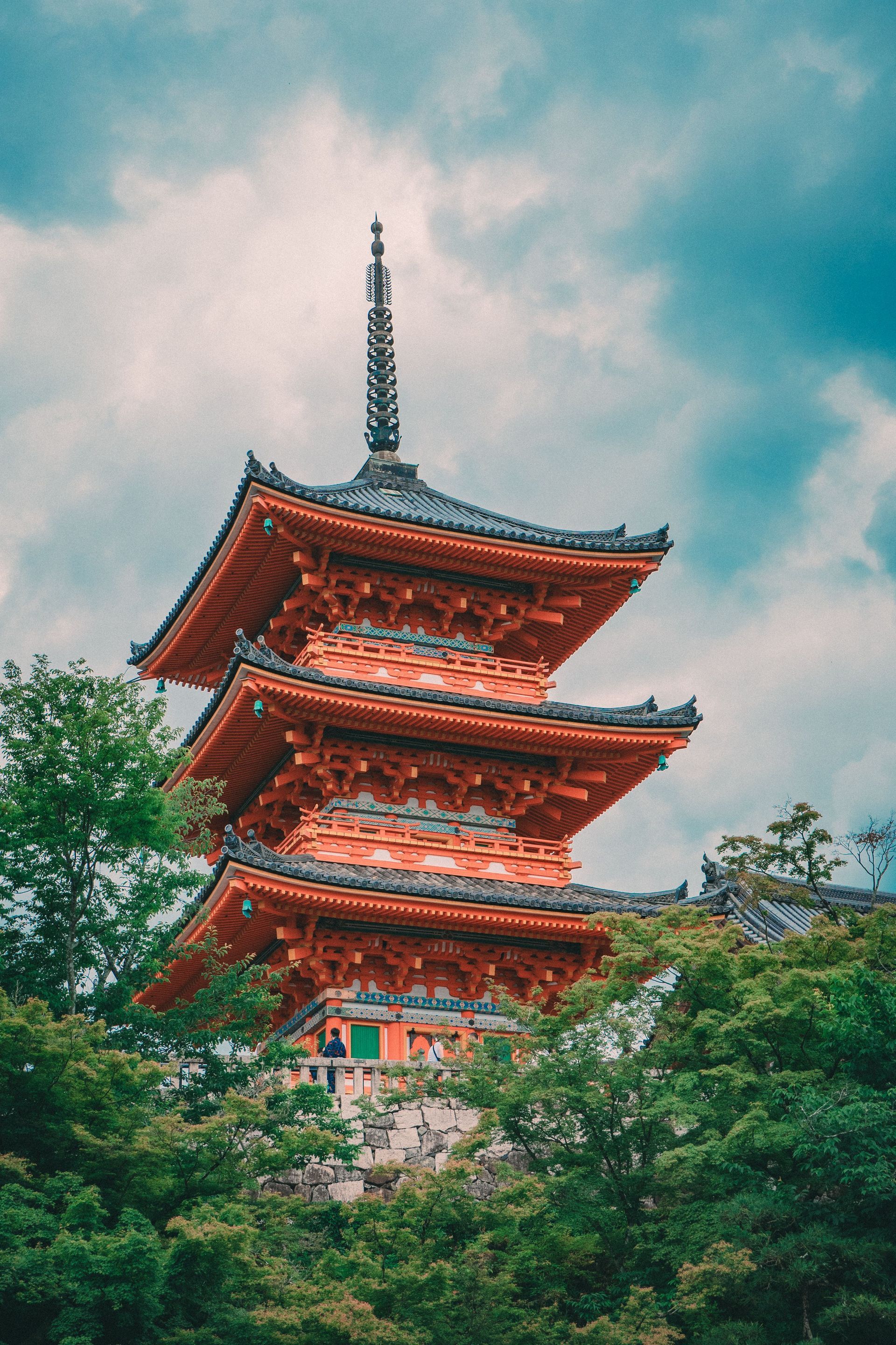 Red pagoda rising above green trees under a cloudy blue sky