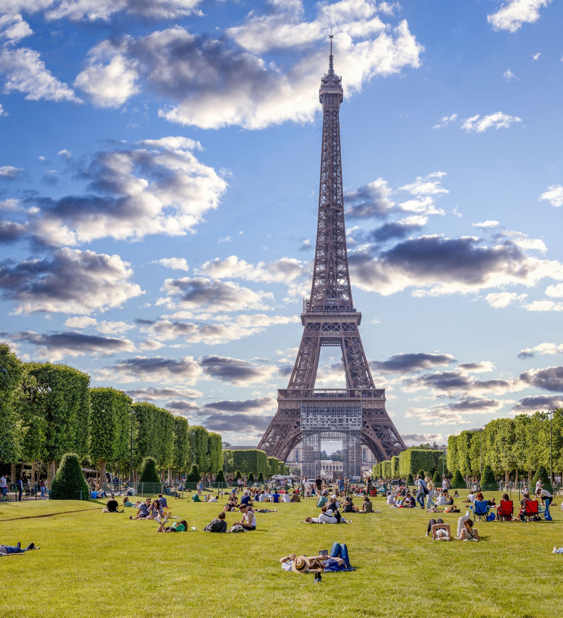 People relaxing on the grass before the Eiffel Tower under a bright, partly cloudy sky