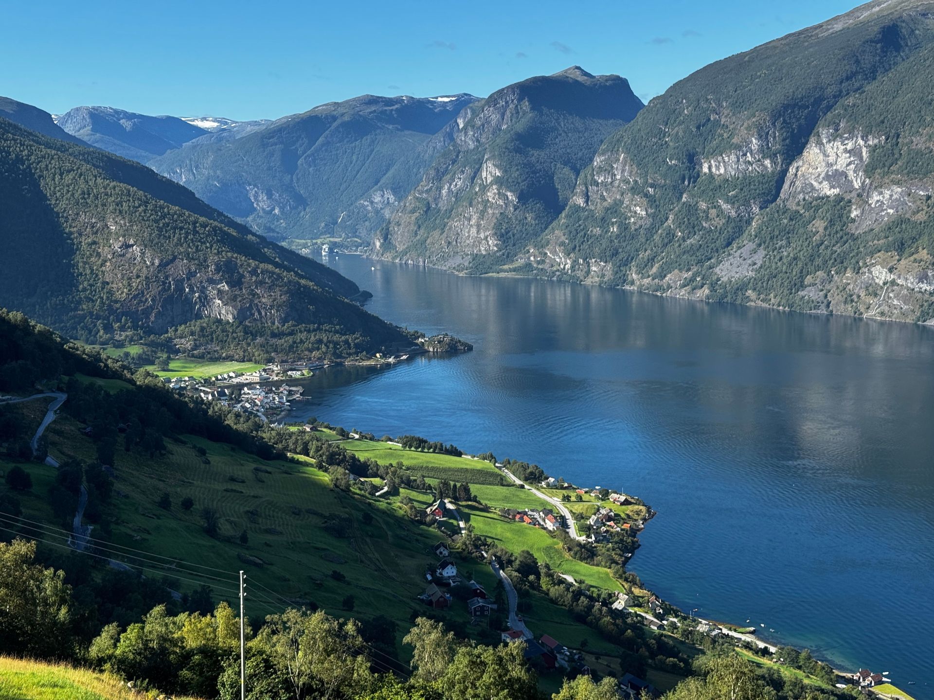 Scenic mountain lake with blue water, green hills, and small lakeside village under a clear sky