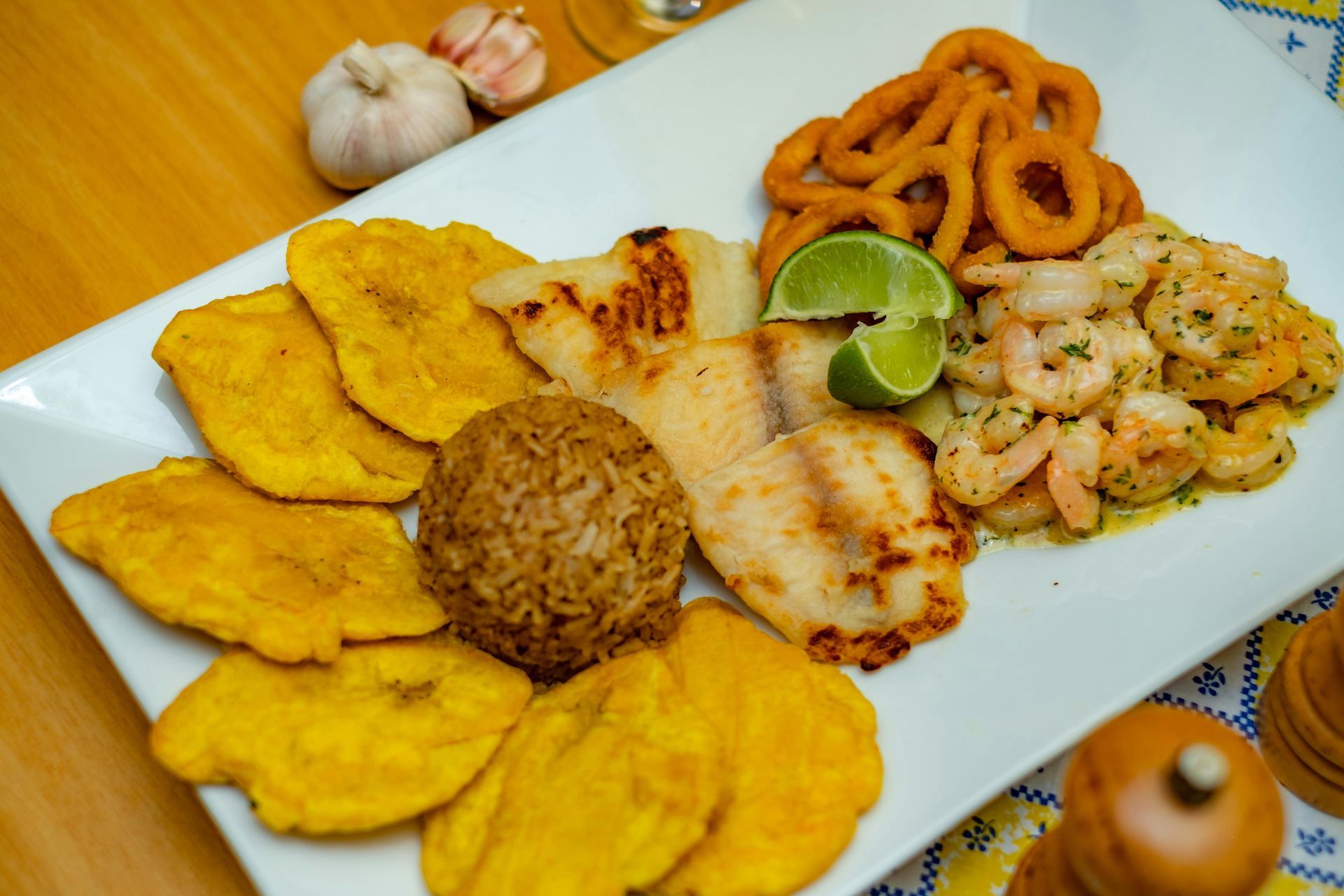 Assorted fried seafood and plantains on a white rectangular plate with lime wedges