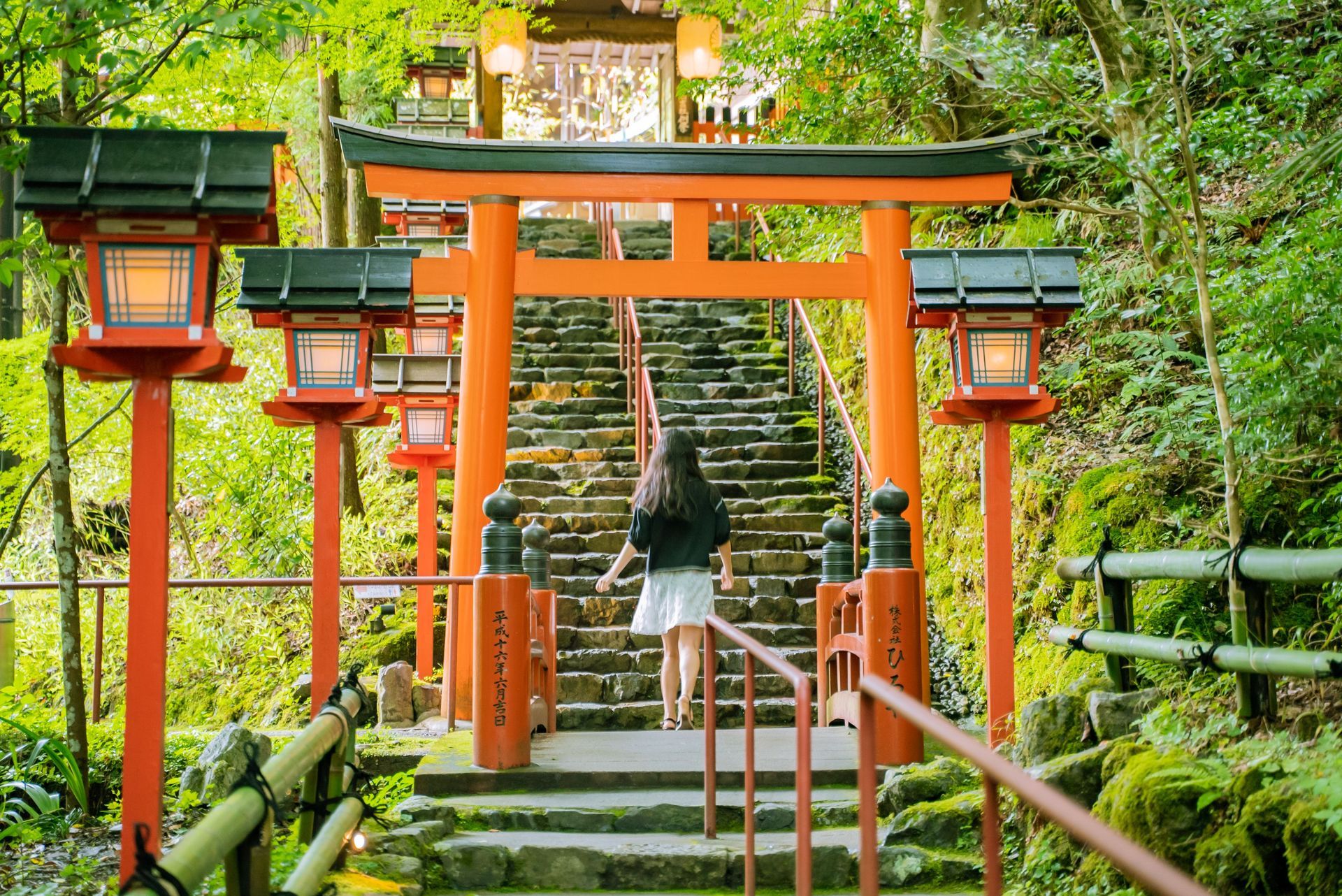 Person on steps beneath orange torii gates in a lush green shrine garden