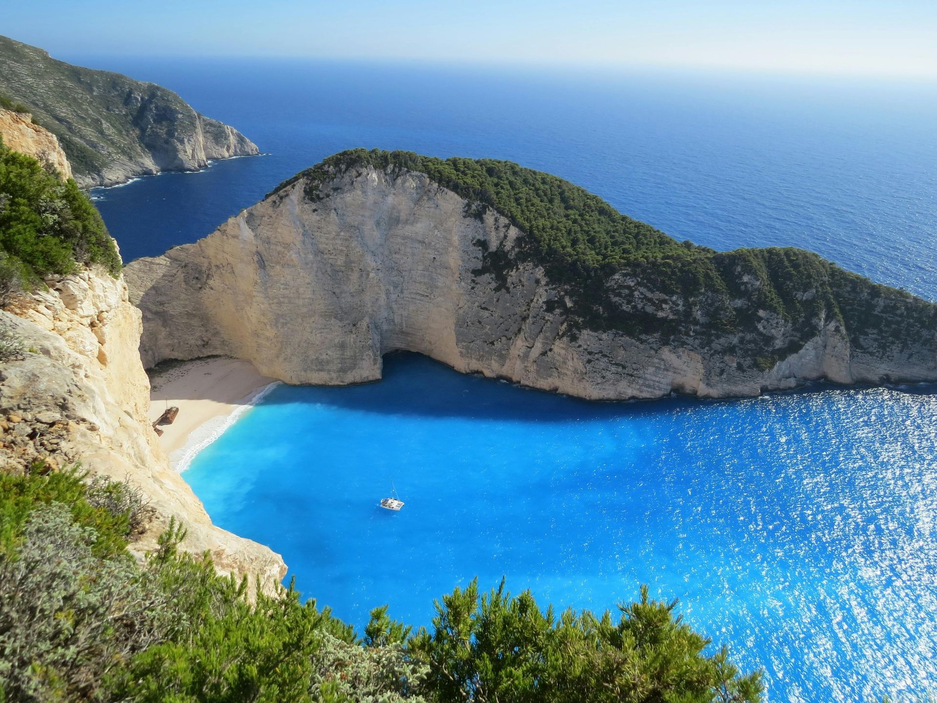 Bright blue cove with white cliffs, green hills, and a small boat on a sunny sea