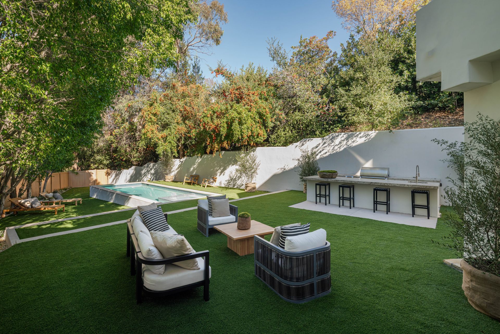 A backyard with a couch , chairs , table and a swimming pool.