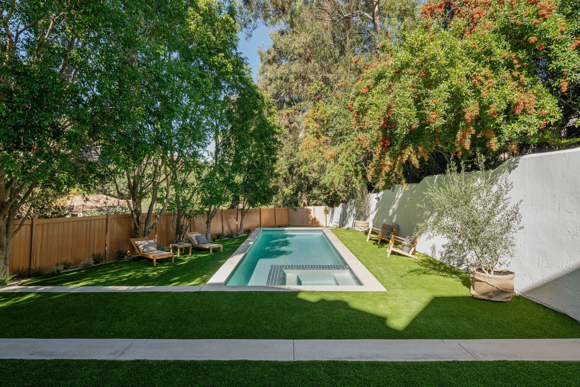 A large swimming pool is surrounded by trees and grass in a backyard.