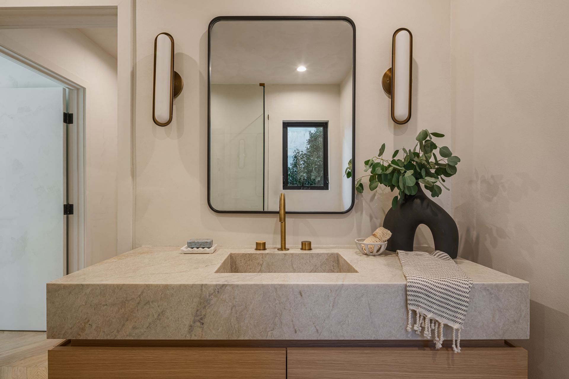 A bathroom with a sink , mirror , and vase.