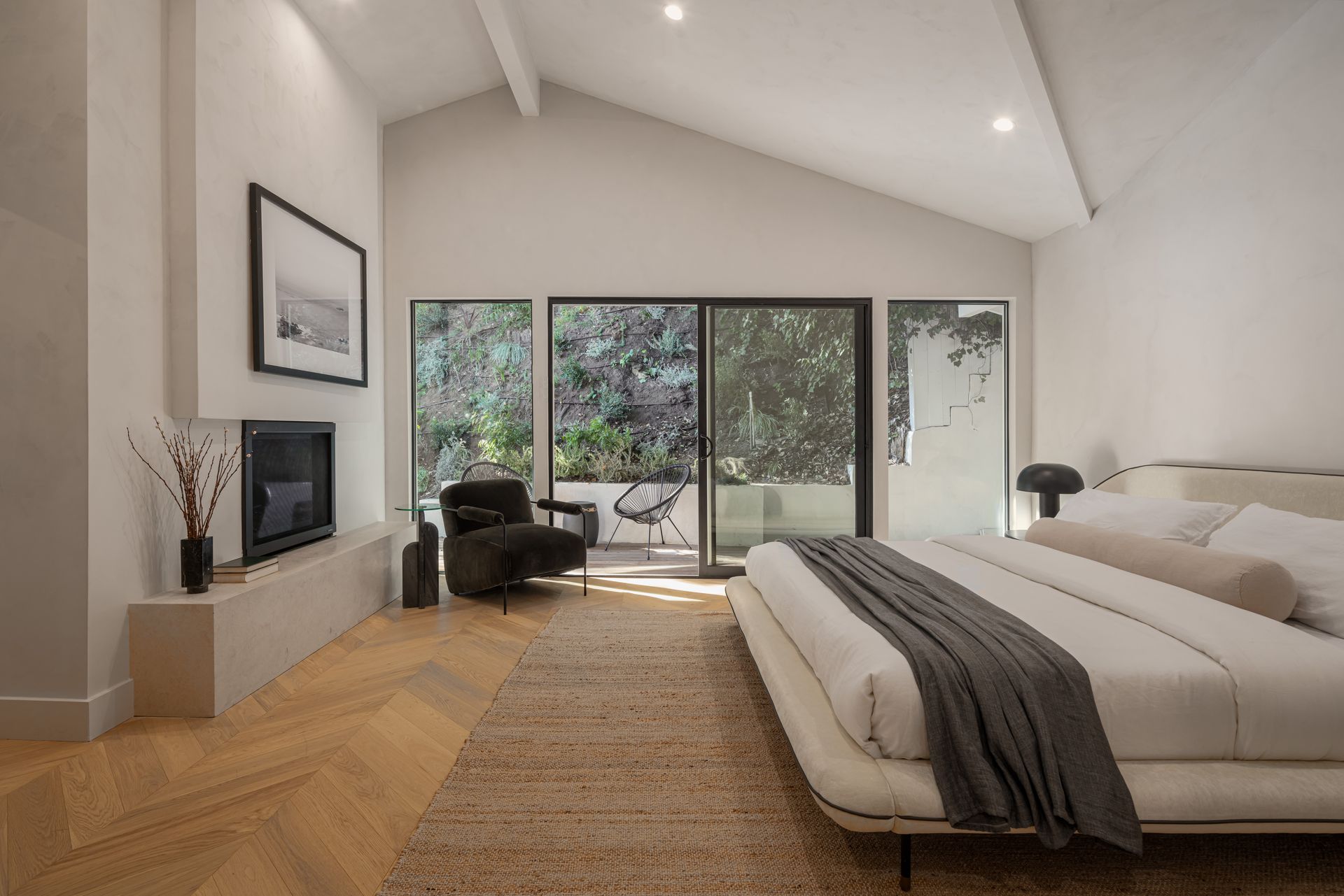 A bedroom with a bed , chair , fireplace and sliding glass doors.