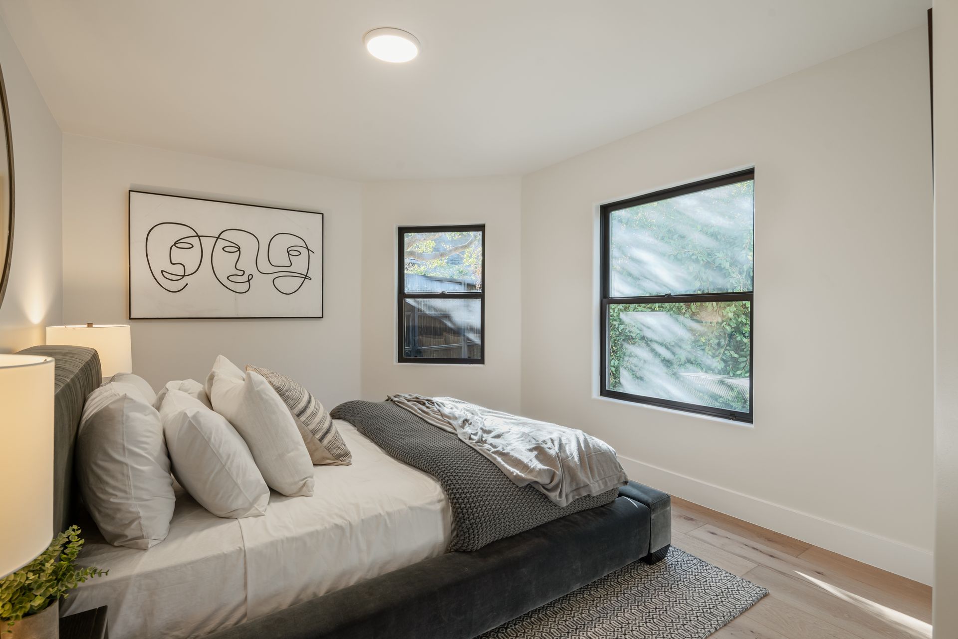 A bedroom with a bed , two windows and a painting on the wall.