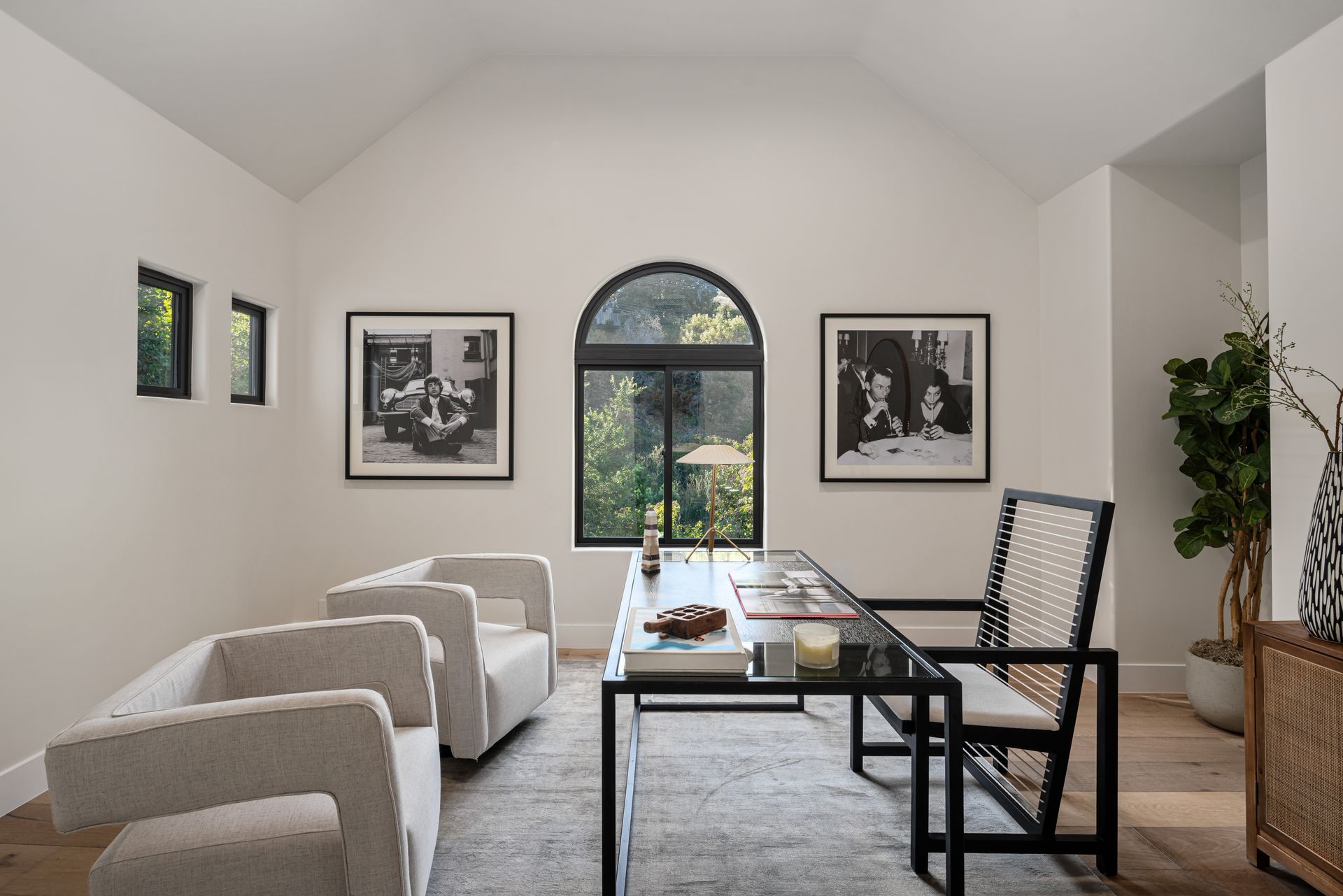 A living room with a desk , chairs , and a large window.