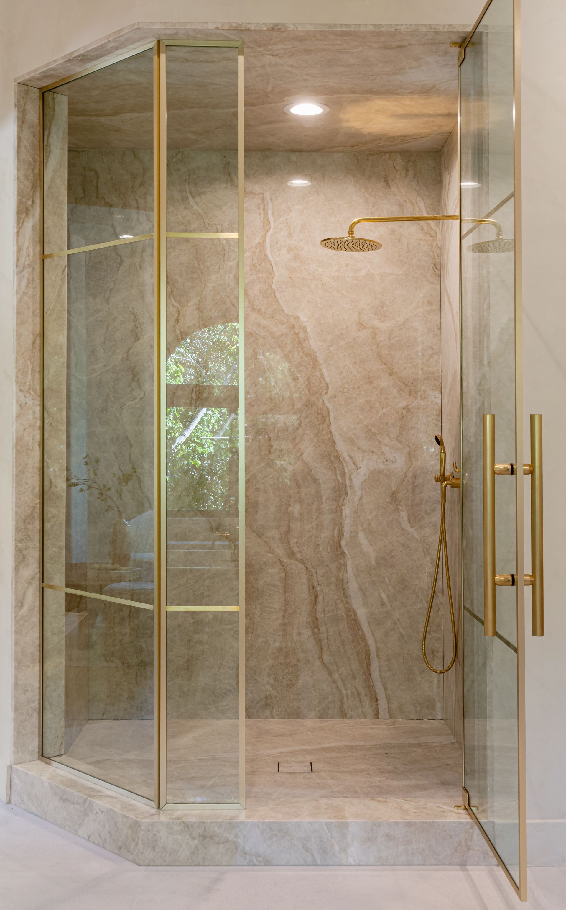 A bathroom with a walk in shower with a marble wall and brass handles.