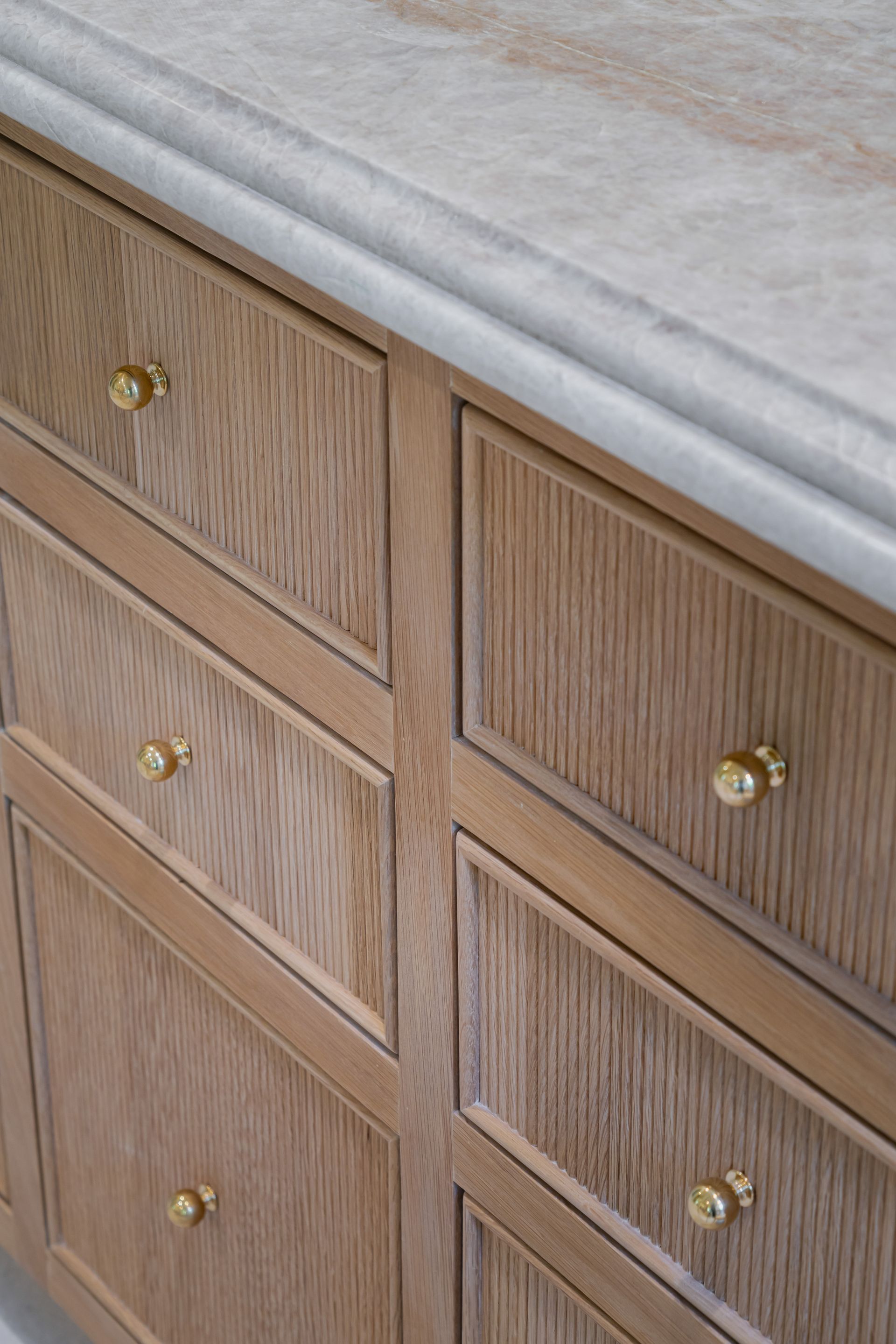 A close up of a wooden cabinet with drawers and a marble counter top.