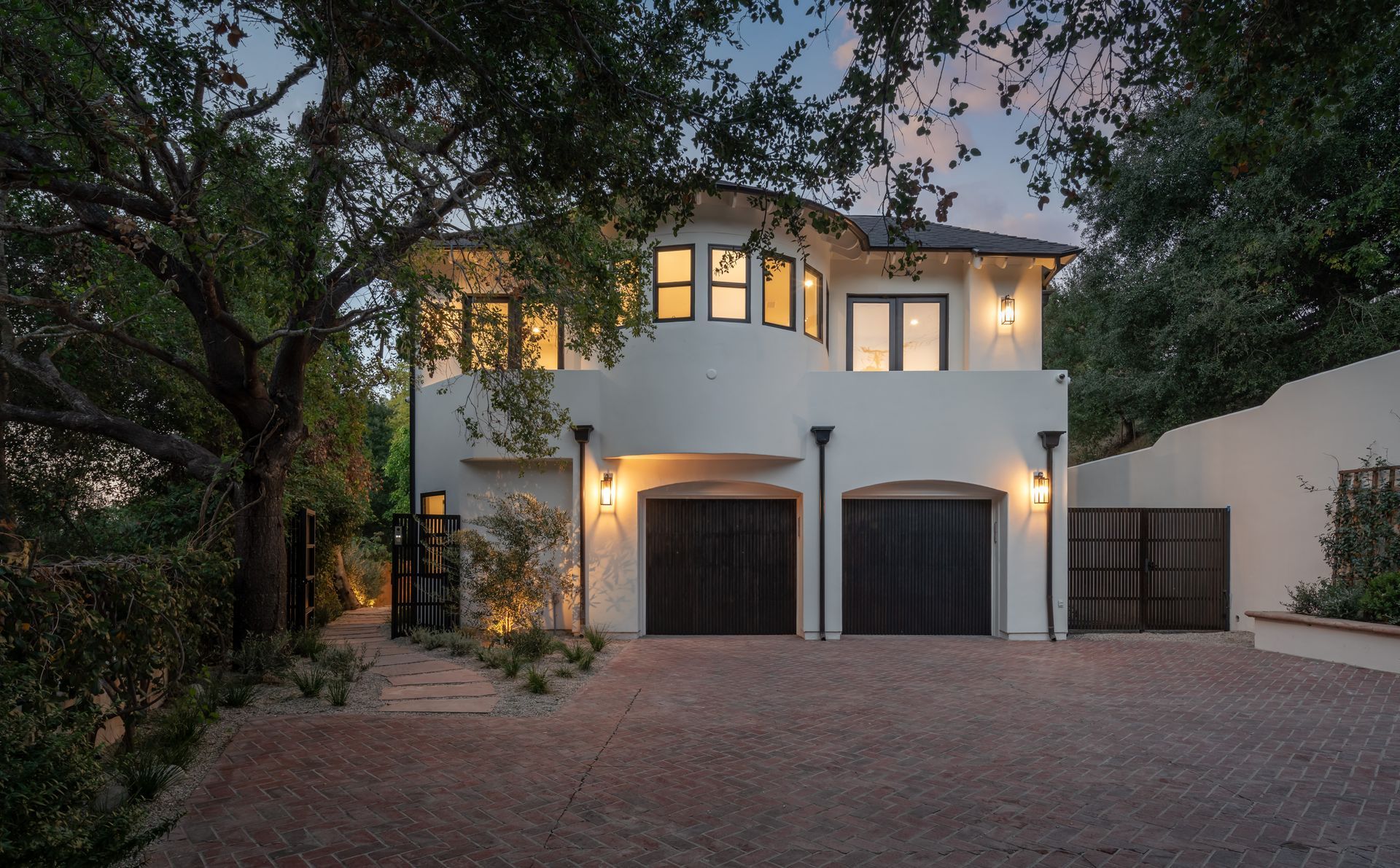 A white house with two garage doors and a brick driveway