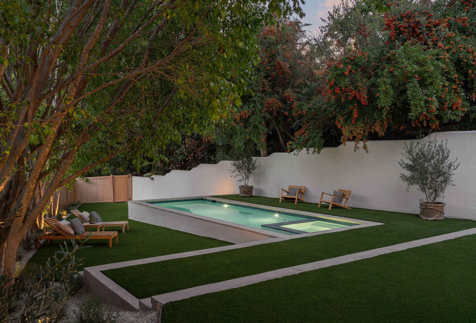 A large swimming pool is surrounded by chairs and trees in a backyard.