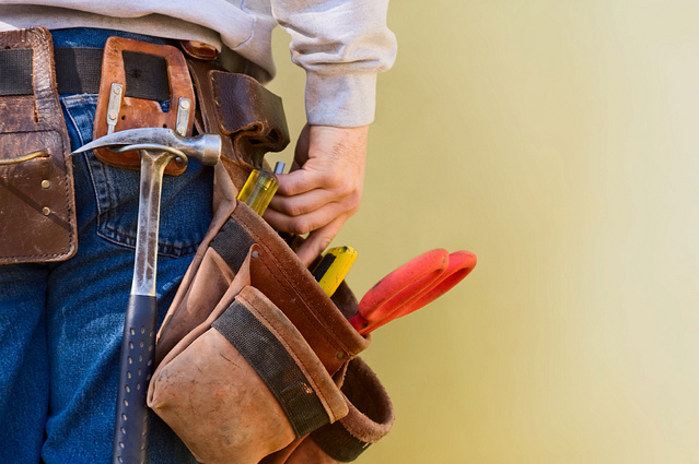 A man is wearing a tool belt with a hammer and screwdriver.