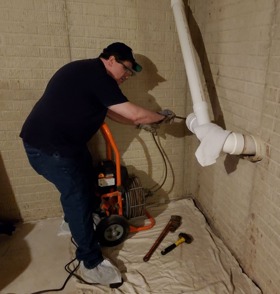 White wall with exposed plumbing pipes, a red valve, and a small wall opening below a slanted ceiling line